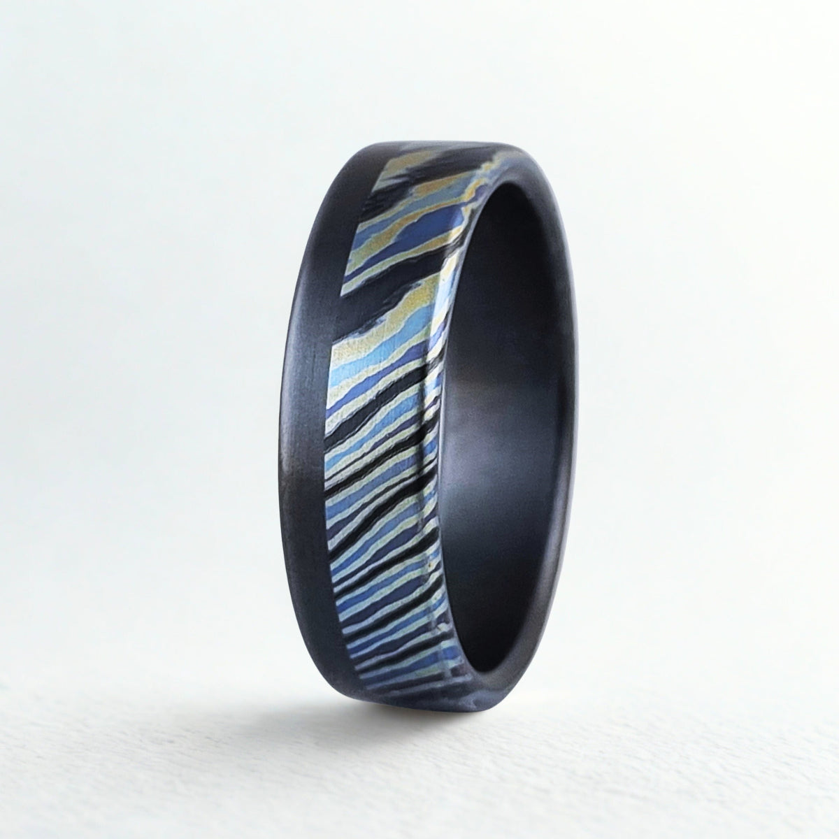 Ring with black band and blue and gold striped pattern on a white background