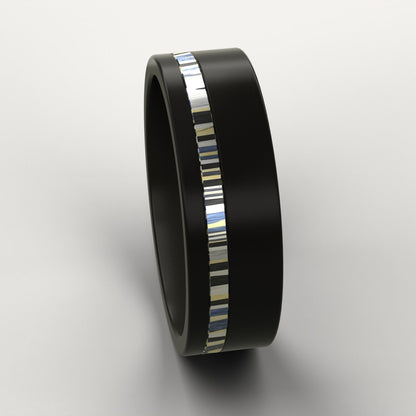 Black ring with a colourful patterned metal inlay on a light grey background